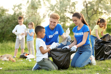 Fototapeta premium Little African-American boy collecting trash with volunteers in park