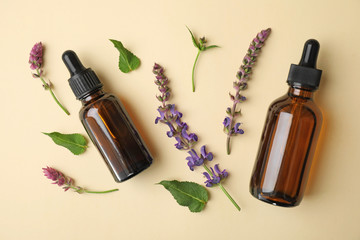 Bottles of essential oil and sage flowers on color background, flat lay