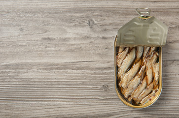 Open tin can of sprats on wooden background, top view. Space for text