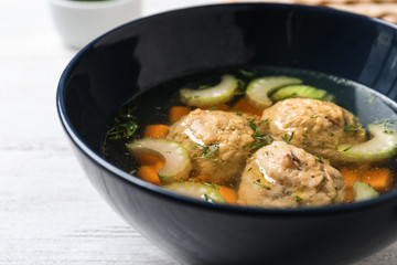 Bowl of Jewish matzoh balls soup on white wooden table, closeup