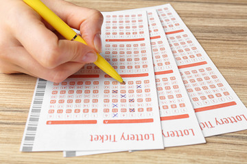 Obraz premium Woman filling out lottery tickets with pen on wooden table, closeup. Space for text