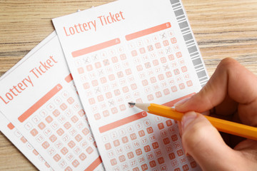 Woman filling out lottery tickets with pencil on wooden table, closeup. Space for text