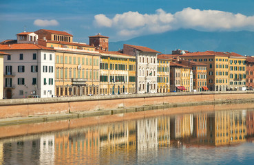 Fototapeta na wymiar yellow facades with wooden windows with traditional green shutters of old Italian houses on the embankment of the river Arno, reflected in the water on a sunny day in the city of Pisa, Tuscany, Italy