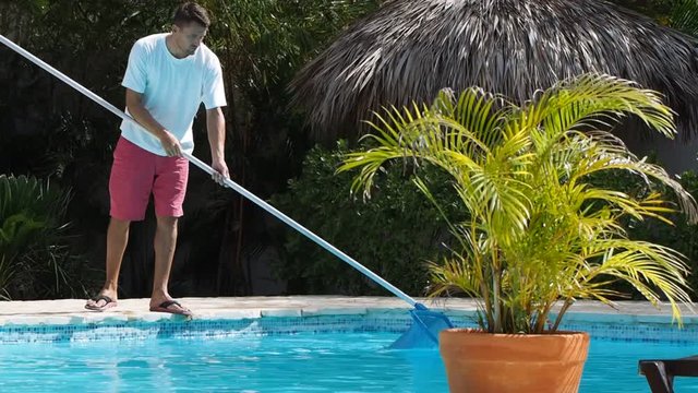 man cleans the swimming pool outside. Tropical island. Summer time.