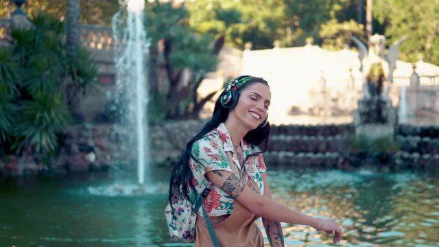 transgender model wearing sunglasses in the green park. She is listening to music with headphones and dancing