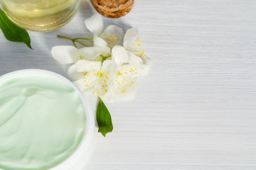 Jar of cream made from natural plant ingredients, oils and herbs, jasmine flowers, on a white wooden background - preparation of organic cosmetics concept, close up, copy space