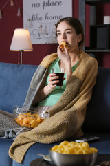 Beautiful young woman eating unhealthy food while watching TV at night