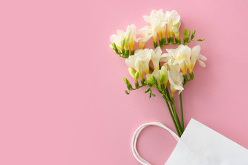 Beautiful freesia flowers and shopping bag on color background