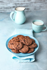 Plate with tasty chocolate cookies, jug and cup of milk on color table