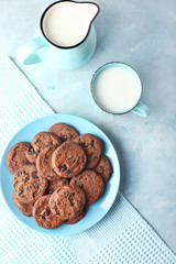 Plate with tasty chocolate cookies, jug and cup of milk on color table