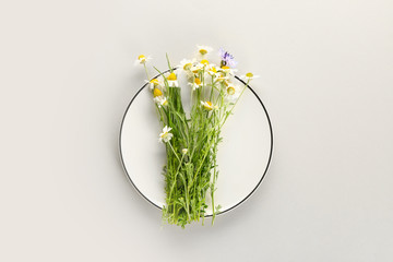 Plate with fresh wild flowers on light background