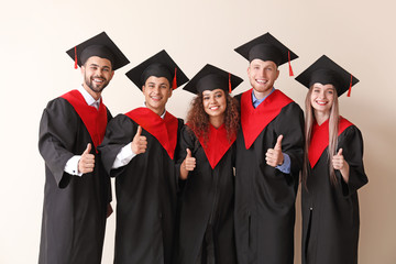 Young students in bachelor robes showing thumb-up on light background