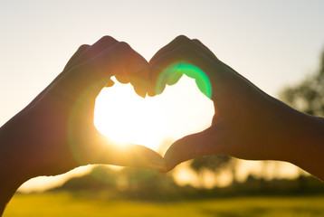 Female hands in the shape of a heart on the background of a beautiful sunset. Hands in the shape of a heart of love