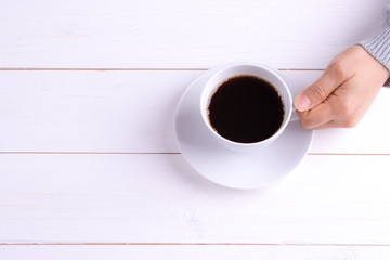 Cup of coffee in female hands on white wooden table. Top view.