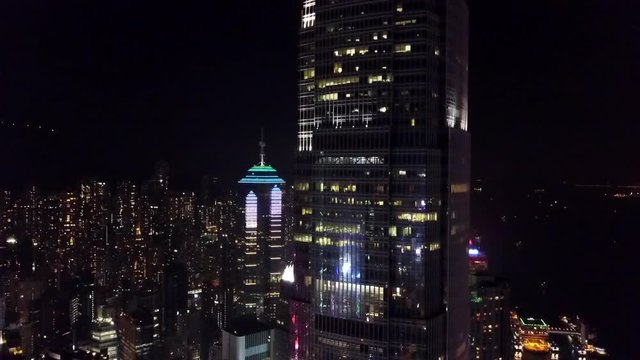 Aerial: Hong Kong Skyscrapers Lit Up at Night with City Behind