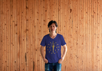 Man wearing Indiana  flag color shirt and standing with two hands in pant pockets on the wooden wall background.