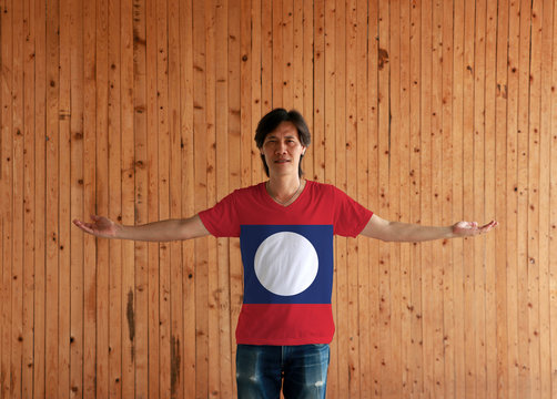 Man wearing Laos flag color shirt and standing with arms wide open on the wooden wall background. - Powered by Adobe