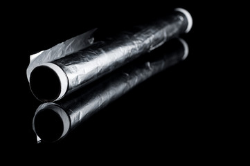 Kitchen foil in a roll on a black background, isolate with reflection on the glass