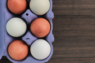 Brown chicken eggs in a blue carton box  on wooden background.. Copy space.
