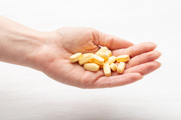Female hand holds yellow pills on a white table background next to a jar. Concept of treatment of recovery and prevention