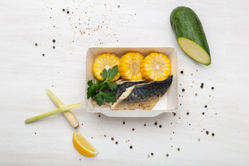 Top view slices of fish and boiled corn lie in the lunch box next to the zucchini leek and corn....