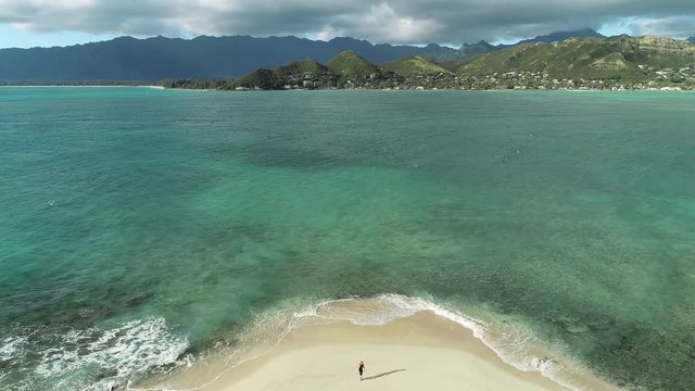 Aerial view of Lanikai beach, Honolulu, Hawaii, low angle view with drone camera vertical pan, person alone on small beach in the middle of a bay, color graded