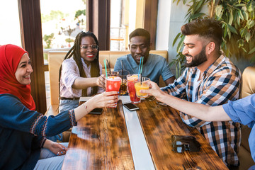 Group of happy friends clinking glasses with juice at cafe.