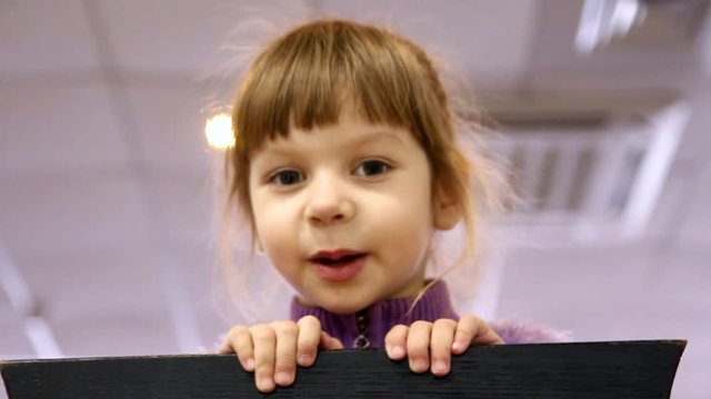 Little Girl Looks Out From Behind A Chair And Grimaces