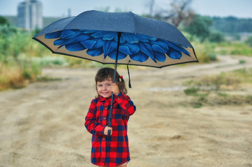 A little girl with an umbrella . The child is holding a large umbrella in the rain .