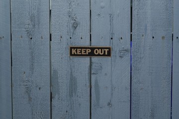 A keep out sign on a blue wood wall.