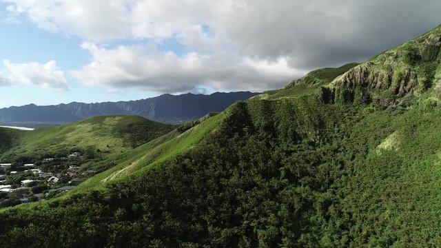 Aerial view of Lanikai beach, Honolulu, Hawaii, low angle view with drone camera moving forward, green mountain ridge with clouds in the background, camera revealing small town