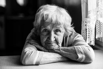 Foto op Plexiglas Close-up zwart-wit portret van een oude vrouw aan de tafel in huis. © De Visu