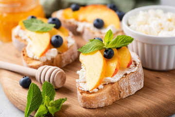 Bruschetta with fruits and soft cheese on wooden cutting board. Closeup view. Toasted baguette bread with soft cheese, peach, honey and blueberries