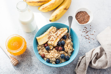 Oatmeal porridge with banana, blueberry, nuts and honey in blue bowl on table. Top view. Concept of clean eating, weight loss, dieting, healthy lifestyle