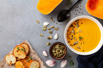 Healthy and delicious autumn pumpkin cream soup in bowl served with seeds and crouton on stone table from above.