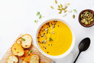 Diet autumn pumpkin or carrot cream soup in bowl served with seeds and crouton on stone table from...