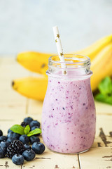 Healthy berry banana smoothie in glass with drinking straw. Vertical orientation. Purple smoothie