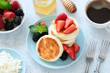 Cottage syrniki with strawberries, honey on blue plate and cup of black coffee on background. Healthy tasty breakfast