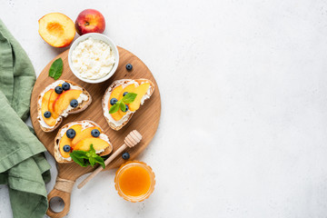 Ricotta and fruit bruschetta. Toasted baguette bread with ricotta cheese, peach, honey and blueberry on wooden board, concrete background. Top view, copy space for text. Healthy summer appetizer or sn - Powered by Adobe