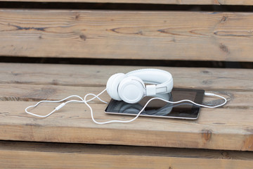 Headphones and a tablet lie on a wooden bench in the park on a warm summer evening. Concept of walk in the summer city park and listening to music and study.