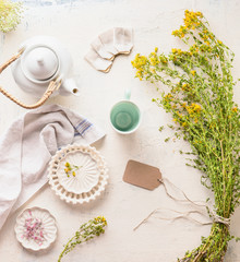White tea set on light table with healing herbs and flowers bunch, top view. Herbal tea with copy...