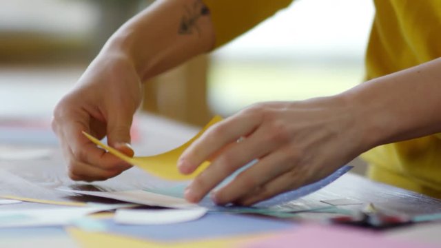 Close up hands of unrecognizable young woman gluing pieces of colored paper when making collage