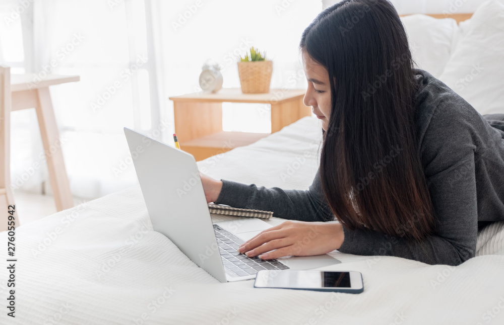 Poster asian woman laying on bed doing paperwork on laptop in bedroom.work at home.e-larning concept.study 