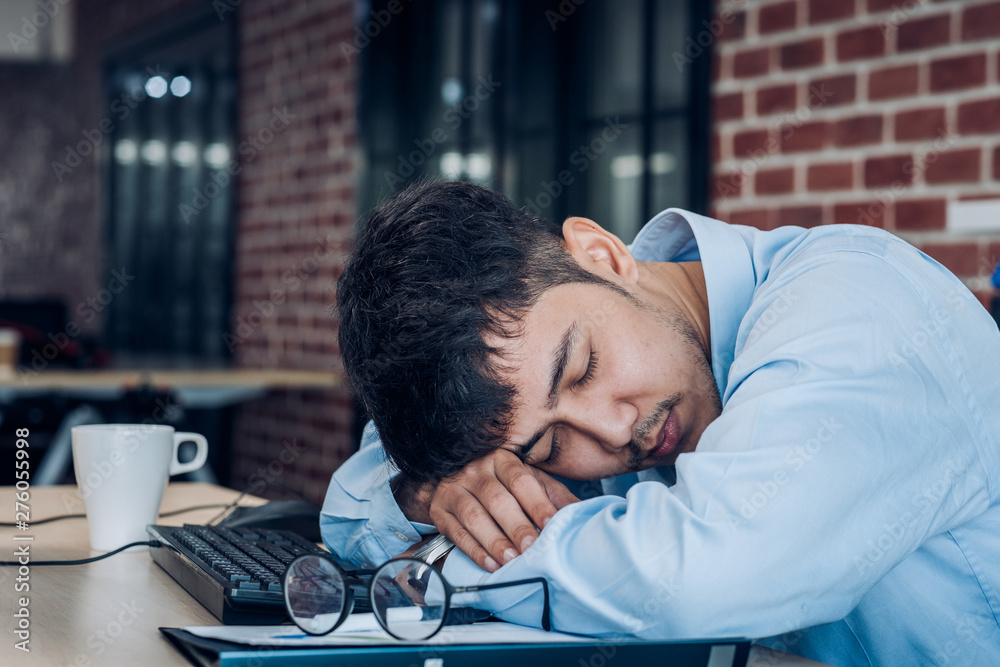 Wall mural Tired asian businessman sleep on working desk table in office.working hard and late.