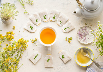 White cup with frame of tea bags and text herbal tea on white table background, top view. Herbal...