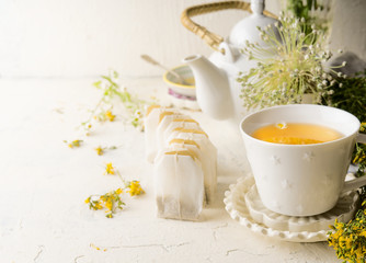 White tea cup with tea bags of herbal tea standing  on white table with teapot and fresh medical...