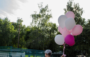 a little boy in the yard holds in his hand a lot of colored balloons
