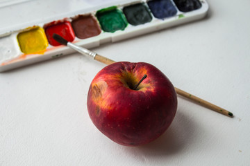 a red apple and watercolor paint and brush on white background