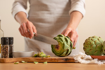 Chef cooks artichoke y slicing it on a light background, concept cooking tasty and healthy food, menu, recipe book, detox, restaurants