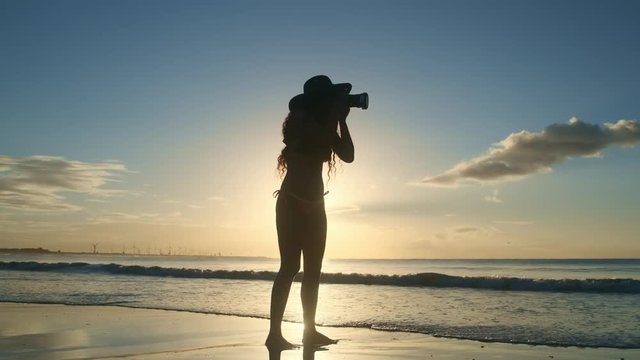 Silhouette of a woman with a camera and sunset near the sea.